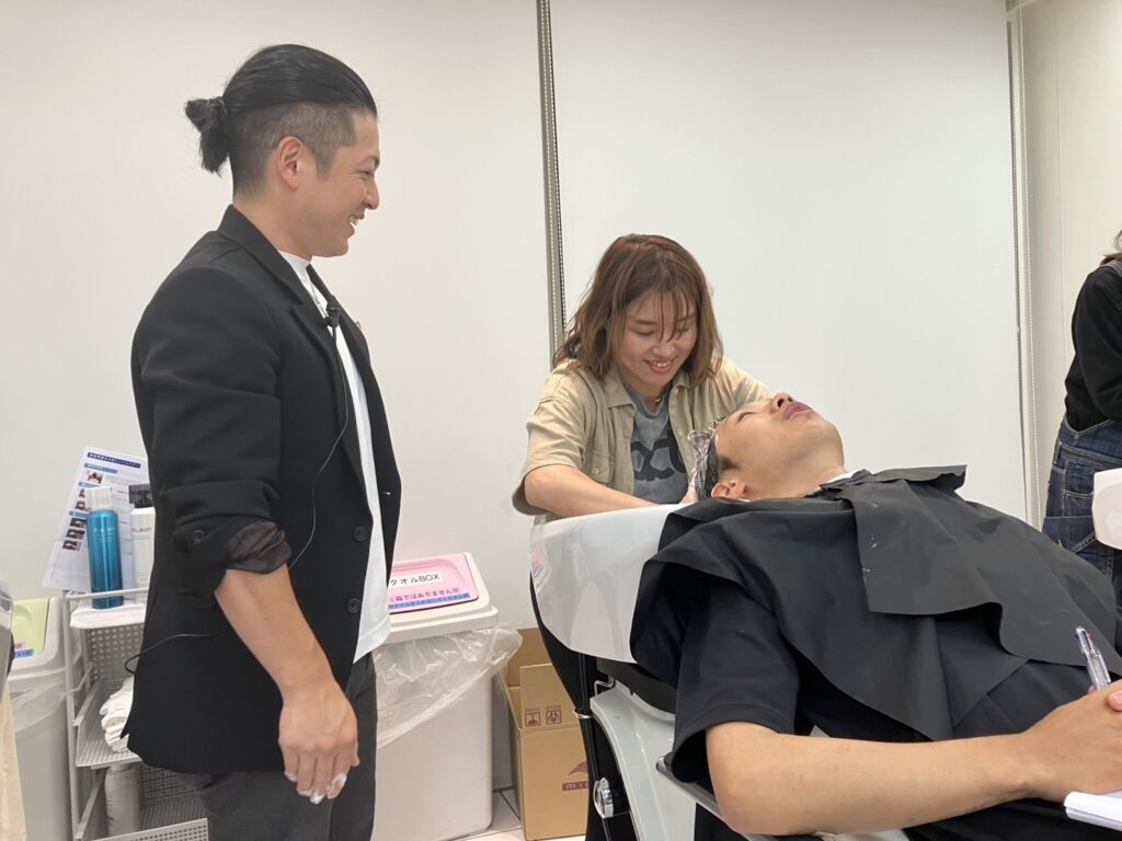 美容師向けヘッドスパ講習で、シャンプー台で施術する受講者の手元を確認する久保鉄平