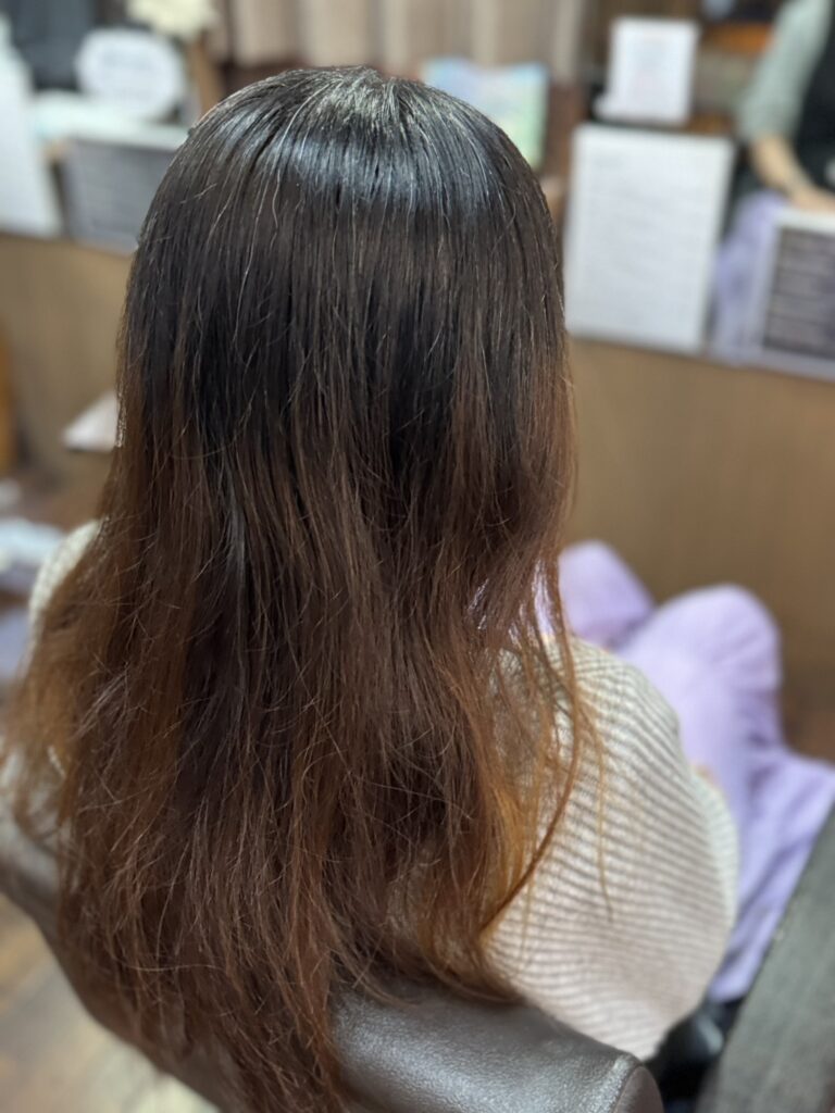 カラー施術前のロングヘア。伸びた暗い地毛と、オレンジみが残る明るい毛先に色の差があり、全体に広がりが見られる状態
